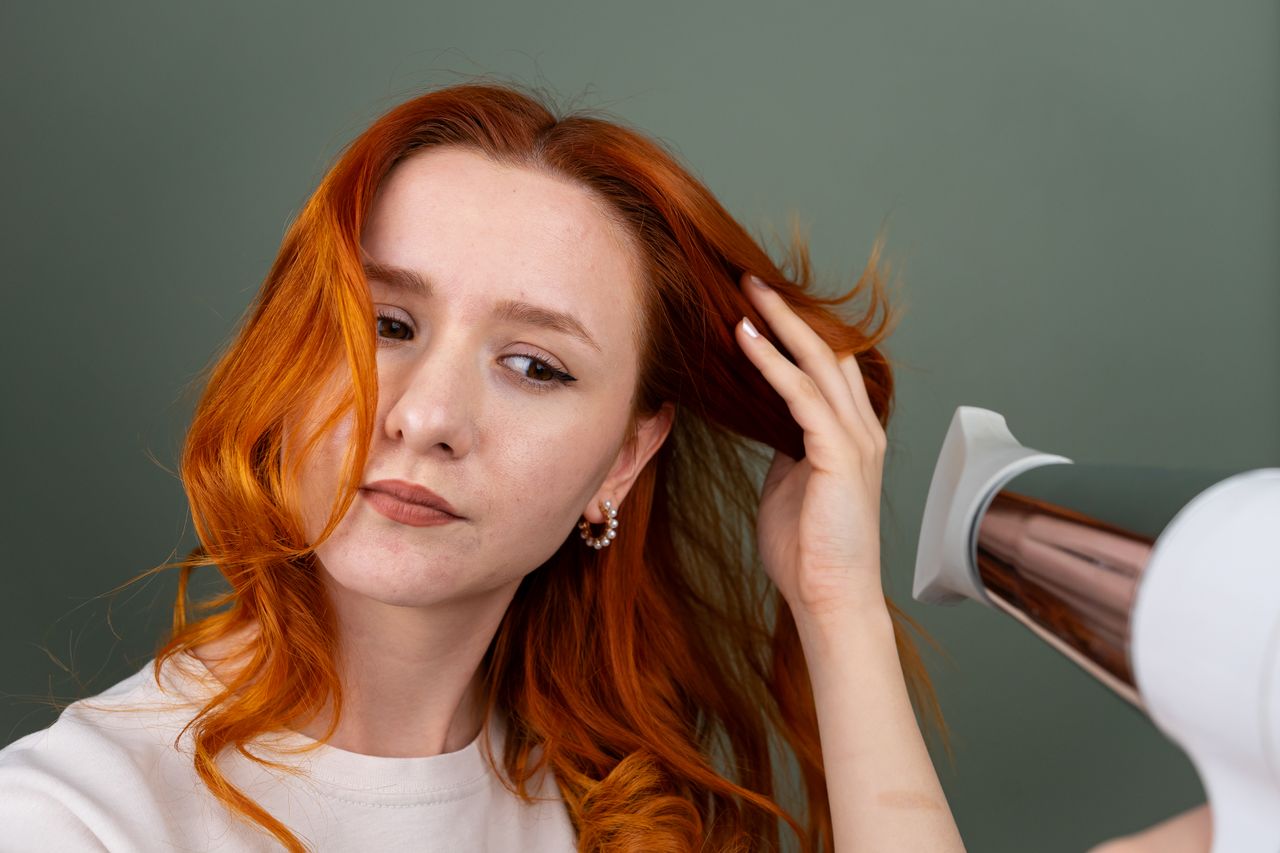Crafting Captivating Headlines: Your awesome post title goes here Close-up of a woman using a hairdryer to style her long red hair indoors.