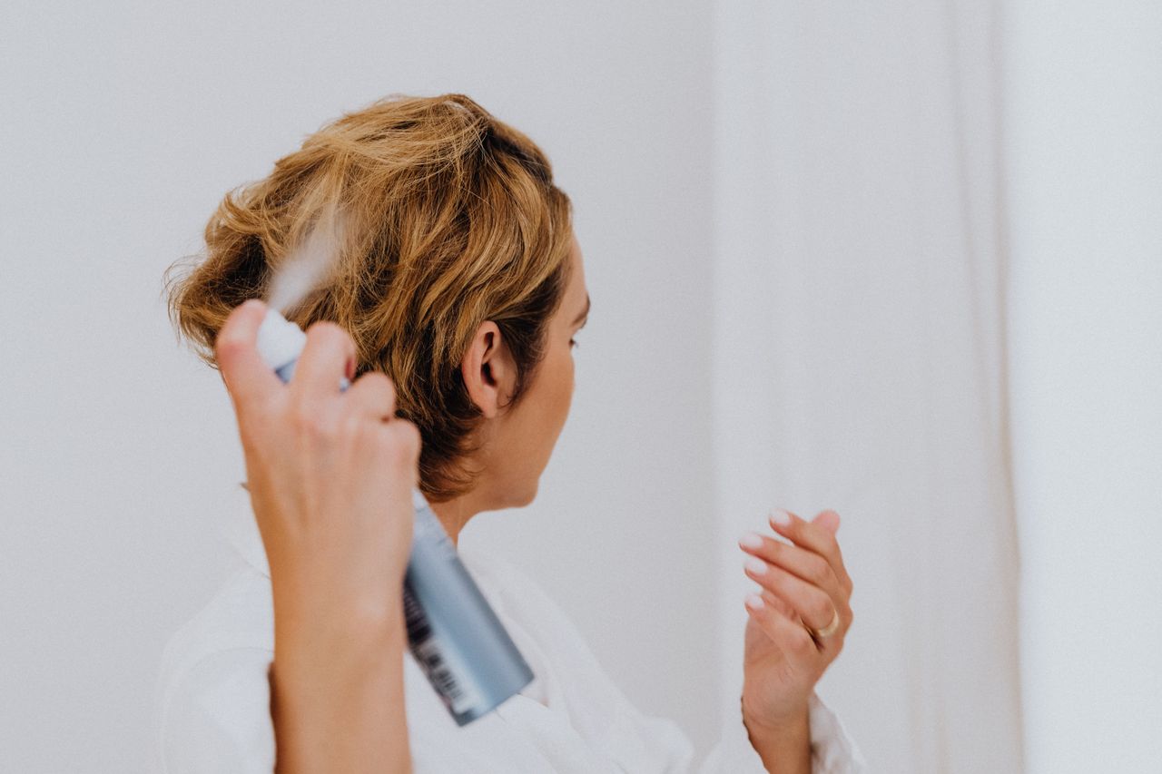 A woman uses hair spray for styling in a bright indoor setting.